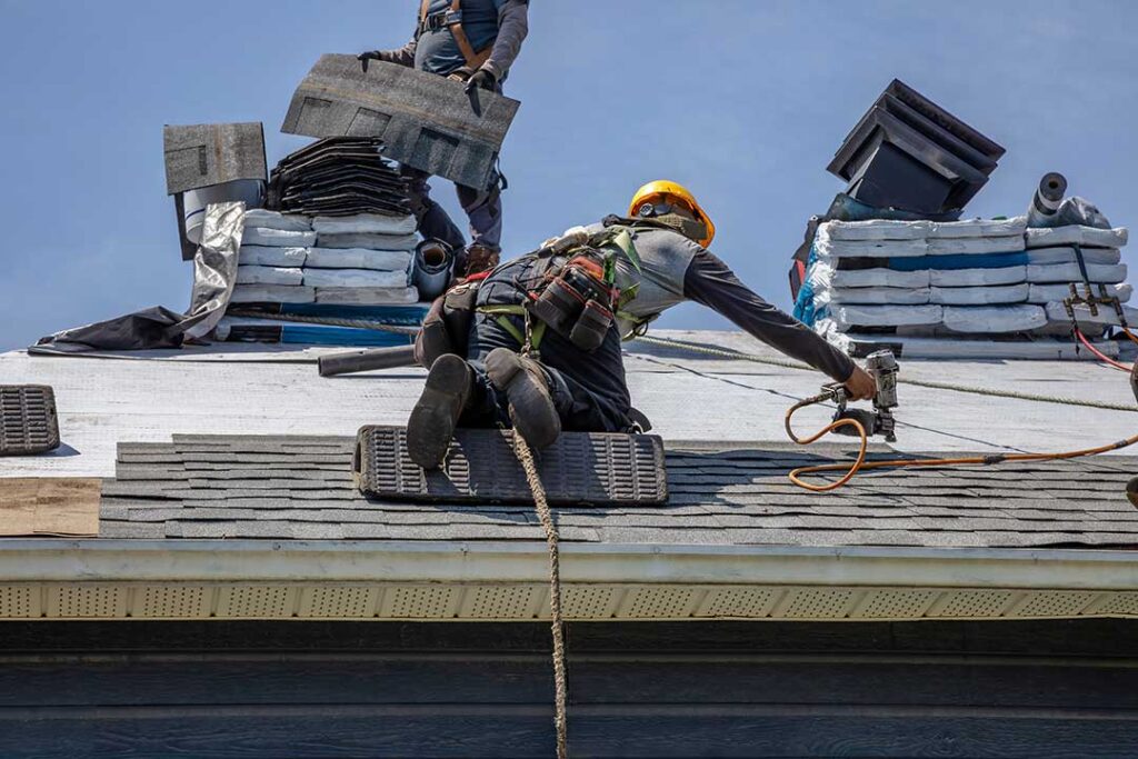 A close-up view of a residential roof with a person inspecting shingles and checking for visible damage.